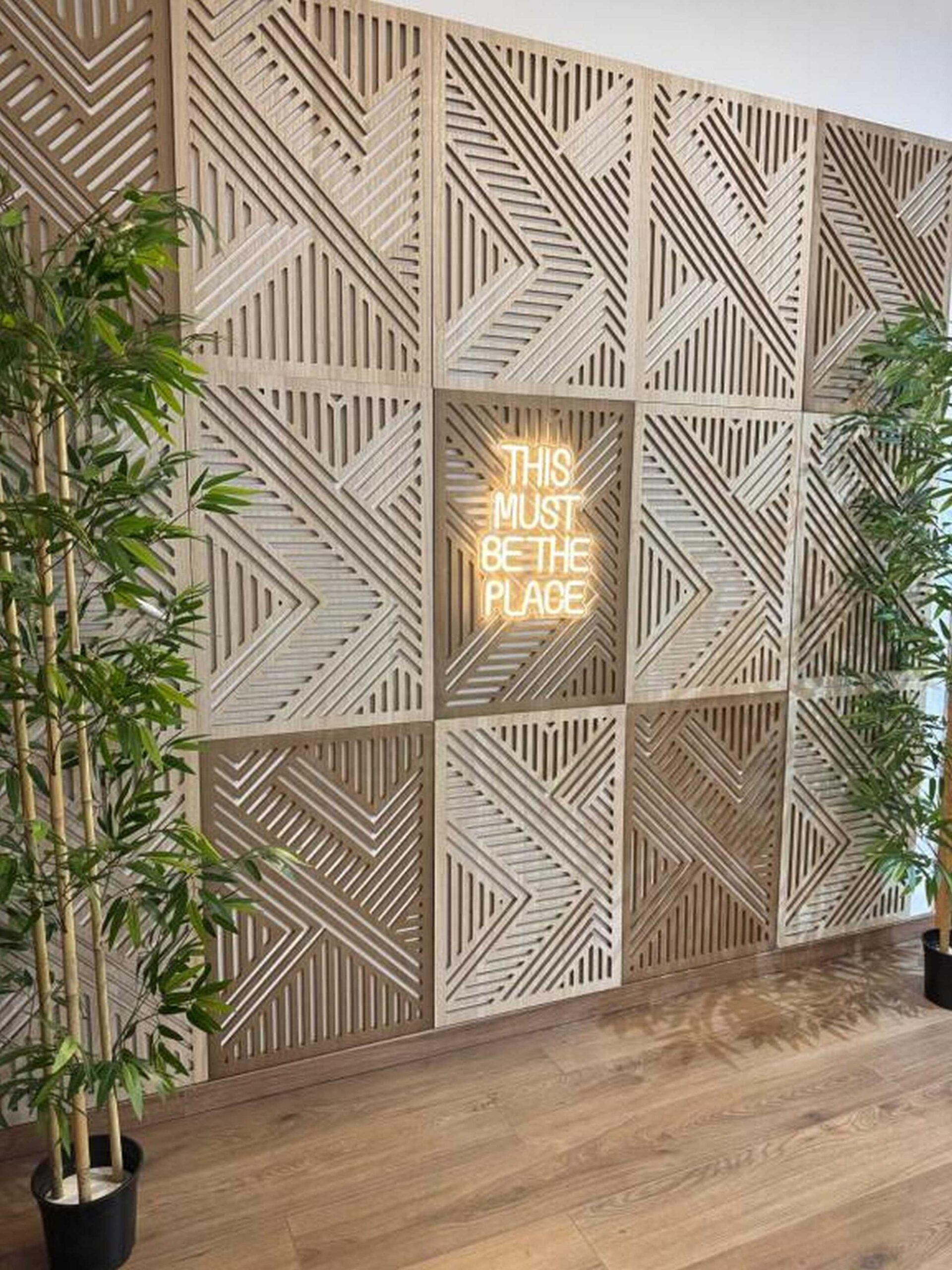 Parete decorativa in legno con scritta al neon “This must be the place” e piante di bamboo
