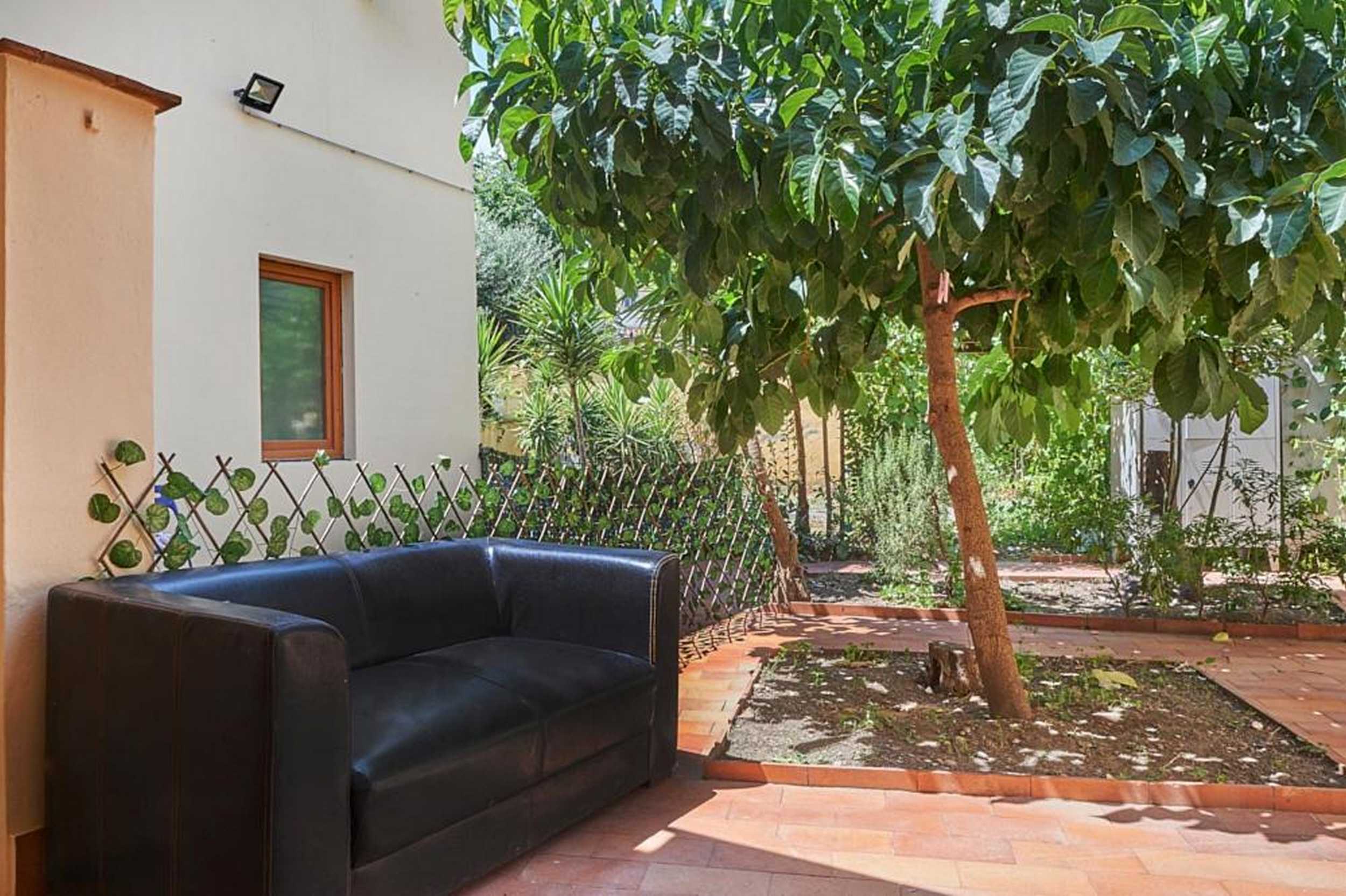 Divano nero in giardino ombreggiato da un albero, spazio esterno riservato per gli ospiti di El Roy Garden Rooms